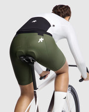Person wearing green cycling shorts and a white top on a bicycle against a white background