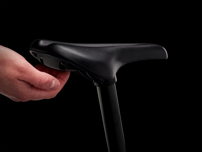 Black bicycle seat held by a hand against a black background