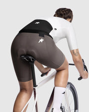 Person wearing cycling shorts and a white jersey on a bicycle against a light gray background