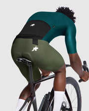 Person wearing green cycling shorts and top on a bicycle with a white background