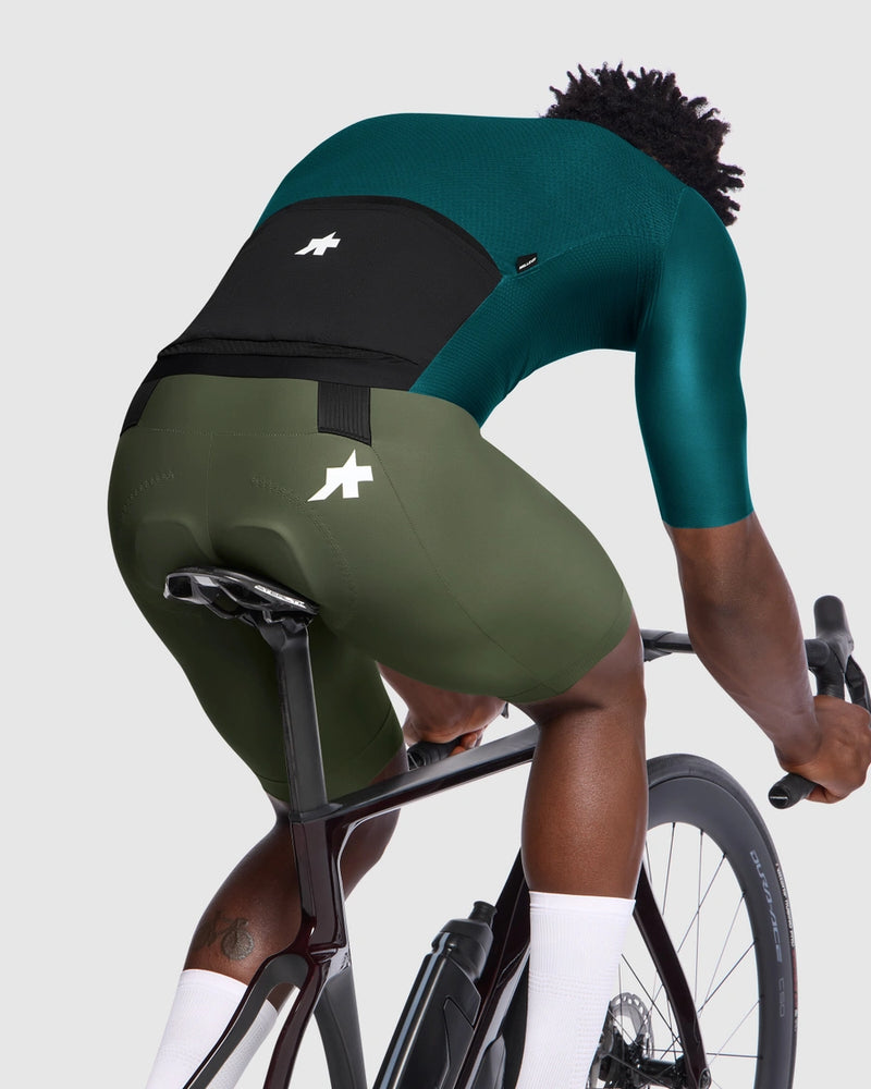 Person wearing green cycling shorts and top on a bicycle with a white background