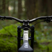 Close-up of a bicycle handlebar with 'ONE' brand name, blurred forest background