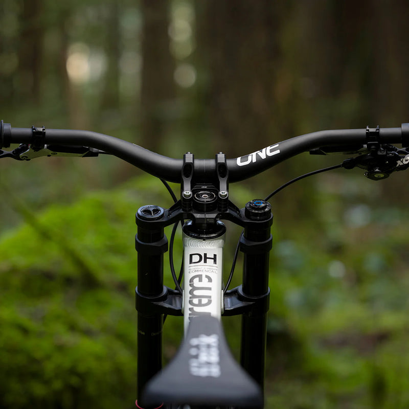 Close-up of a bicycle handlebar with 'ONE' brand name, blurred forest background