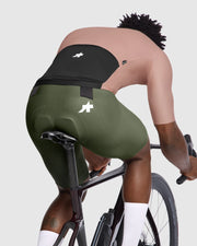 Person riding a bicycle wearing green cycling shorts with a visible brand logo.