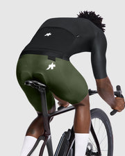 Person riding a bicycle wearing green and black cycling shorts on a light gray background