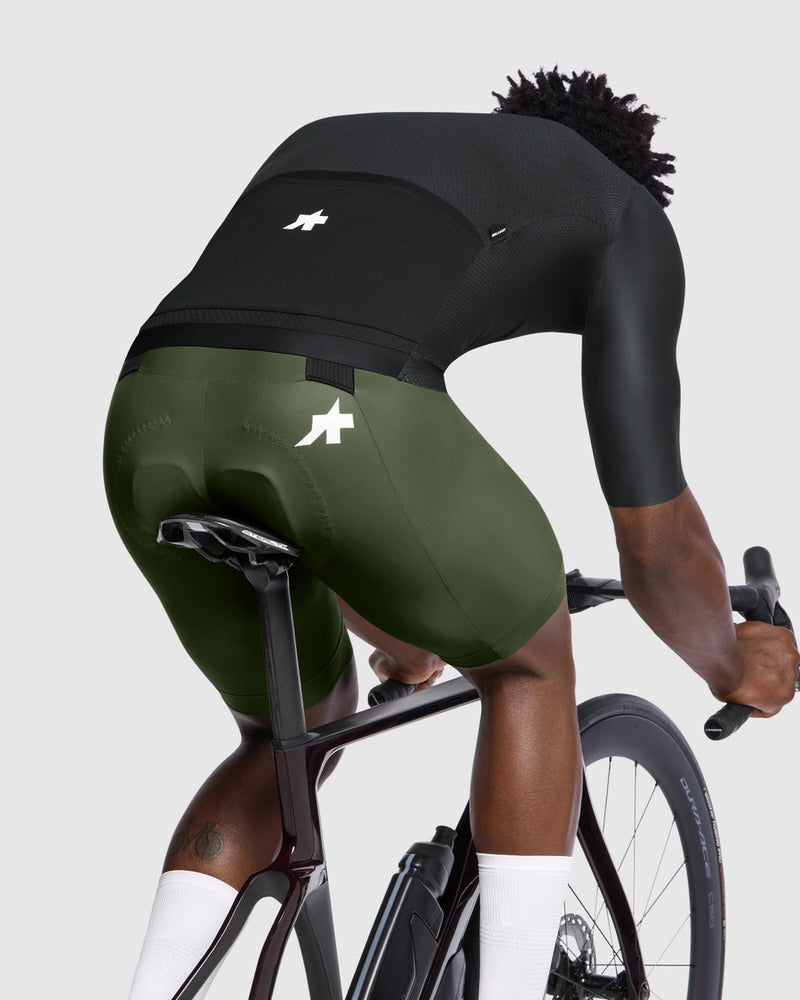 Person riding a bicycle wearing green and black cycling shorts on a light gray background