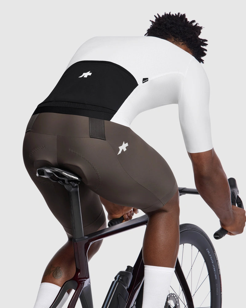 Person wearing a white cycling jersey and brown shorts on a bicycle against a light gray background