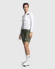 Person wearing a white long-sleeved jacket and green shorts on a light gray background