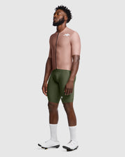 Man wearing a beige cycling jersey and green shorts on a white background