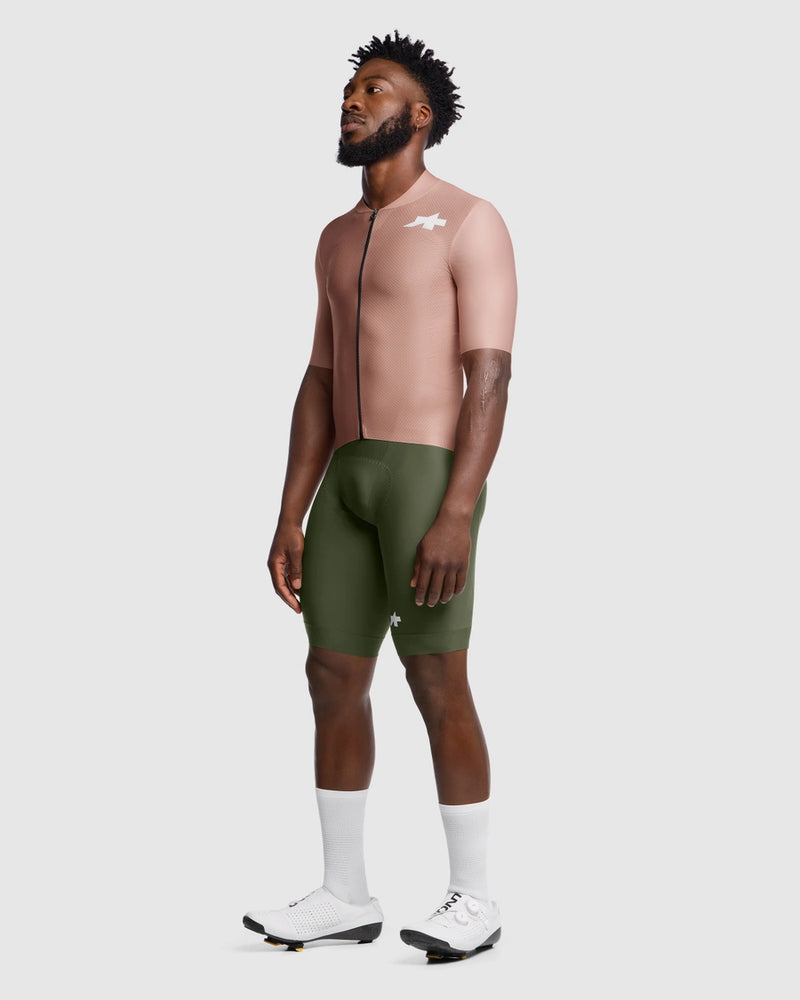 Man wearing a beige cycling jersey and green shorts on a white background