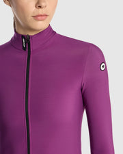 Close-up of the Assos UMA GT Spring Fall LS Jersey C2 in Purple Alchemy on a female cyclist, showing the mock neck with UMA GT detail and ASSOS logo on the upper arm