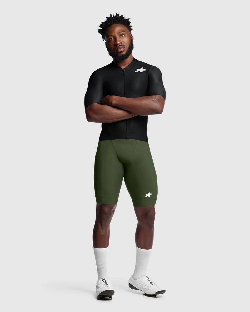 Person wearing a black cycling jersey and green cycling bib shorts on a white background
