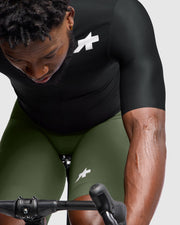 Person wearing a black and green cycling outfit with a brand logo on a white background