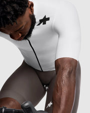 Person wearing a white cycling outfit with a black logo on a light gray background