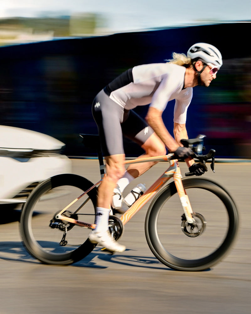 Cyclist in a white outfit and helmet riding a bamboo bike on a road with blurred background