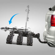 A black 3-bike hitch-mounted car carrier rack shown attached to the rear of a silver vehicle on a light gray studio background, with a blue arrow indicating mounting orientation.