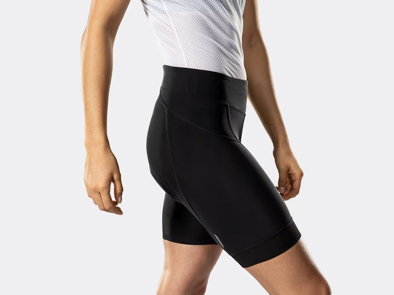 Bontrager Anara women's black cycling shorts side profile on model, highlighting the wide waistband, ergonomic multi-panel design, reflective leg accents, and stretch-fit construction for natural pedalling movement.