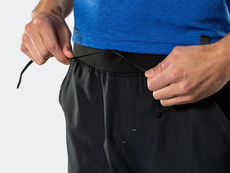 Close-up view of the waistband on black Bontrager Quantum shorts with the t-shirt lifted as the model adjusts the integrated drawstring cords