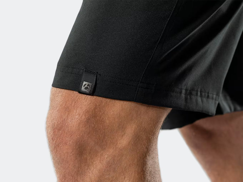 Close-up view of the lower hem on the black Bontrager Quantum shorts hitting near the knee, highlighting the subtle reflective Bontrager logomark