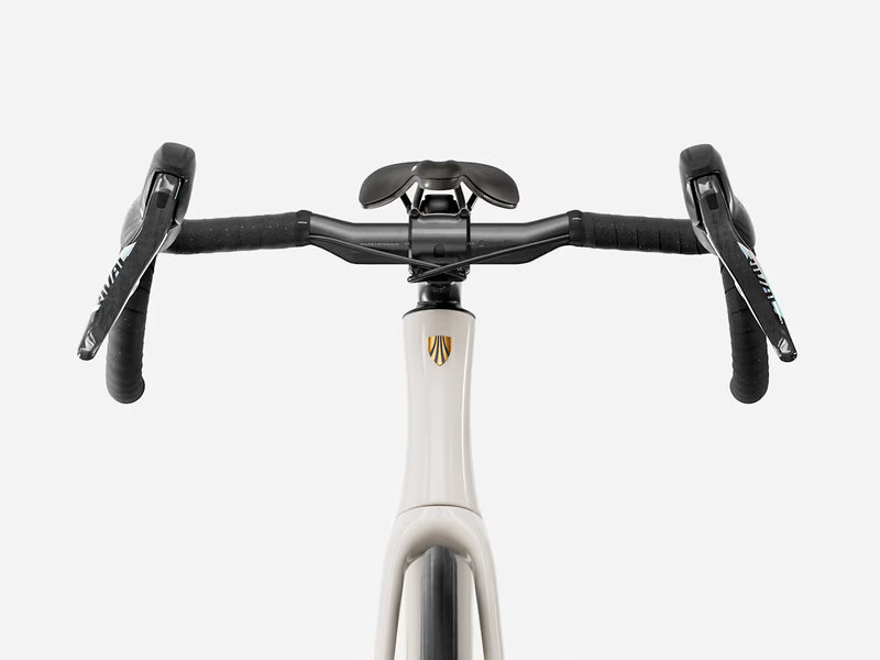 Close-up of an endurance road bicycle drop handlebar with black handlebars and levers attached to a white frame with a gold shield logo, on a light gray background.