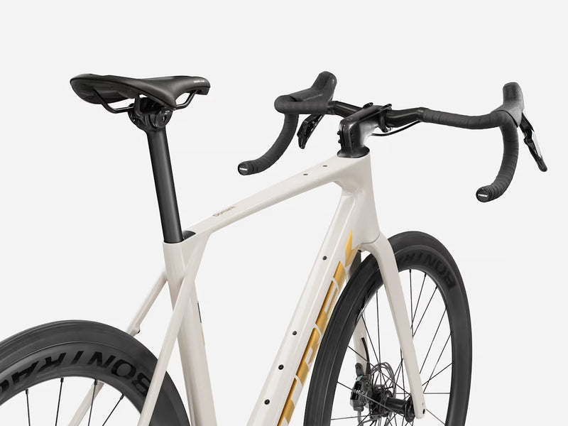 Close-up of an endurance road bicycle frame and handlebars in off-white with gold branding and black components, including the saddle, handlebar grips, and wheels.