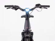 Front view of a black electric bicycle with a bright white front light illuminated, set against a clean white background.