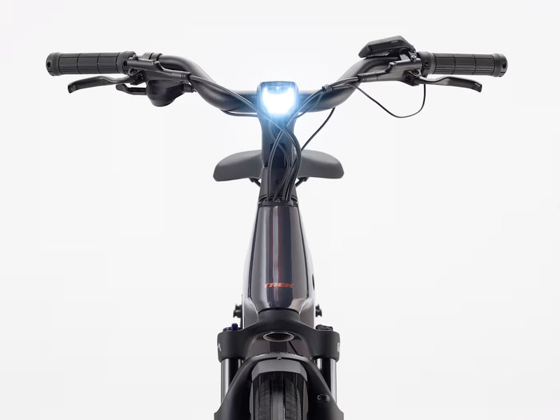 Front view of a black electric bicycle with a bright white front light illuminated, set against a clean white background.