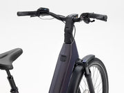 Close-up of an electric bicycle handlebar and frame, showing black grips, a digital display, and a dark metallic purple frame against a clean white background.