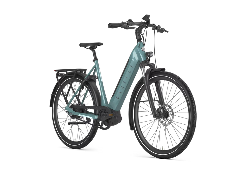 A low step electric bicycle in a muted teal color with black components, shown from a three-quarters front angle on a solid white background. The brand name 'GAZELLE' is printed vertically on the downtube.