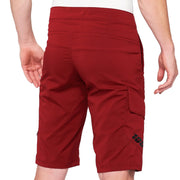 Rear product view of brick-red 100% Ridecamp mountain bike shorts featuring back waistband stitching, prominent 100% logo branding, and side cargo pocket