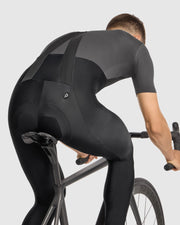 Person wearing a black cycling outfit riding a bike on a light gray background