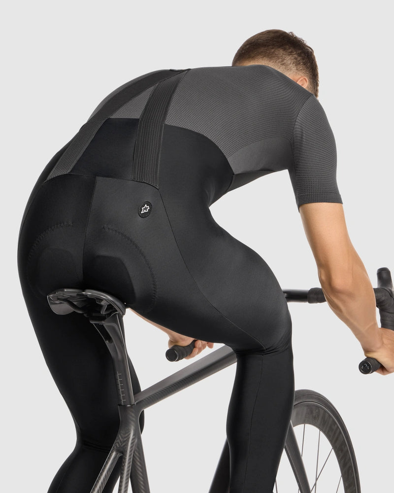 Person wearing a black cycling outfit riding a bike on a light gray background