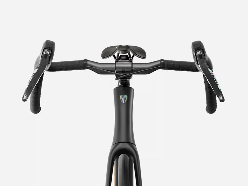 Close-up of a black drop handlebar endurance road bicycle setup with a black saddle and black handlebar tape, shown against a light gray studio background. A small blue and white shield logo is visible on the handlebar stem.