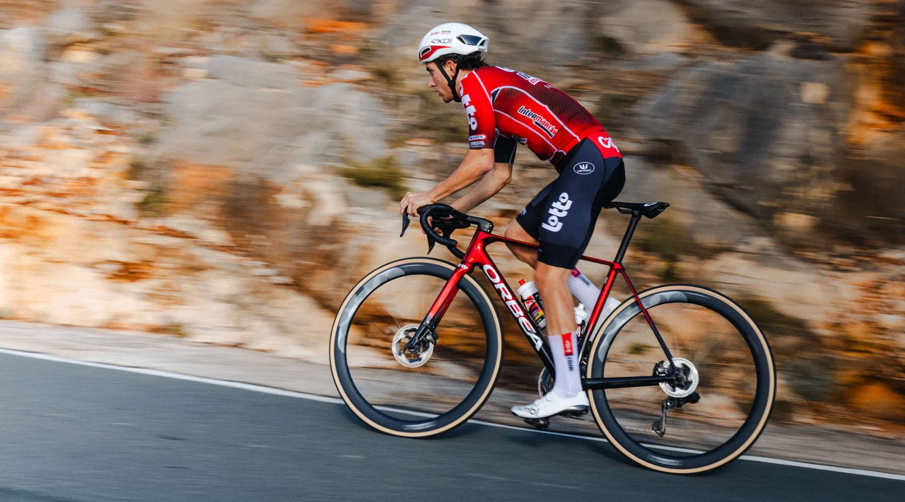 Cyclist in a red and black outfit riding a bicycle on a road with a blurred natural background