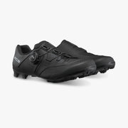Three-quarter view of paired black Shimano SH-XC503 off-road shoes highlighting the lateral BOA dial dial on one shoe and smooth medial construction on the other