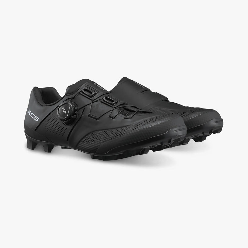 Three-quarter view of paired black Shimano SH-XC503 off-road shoes highlighting the lateral BOA dial dial on one shoe and smooth medial construction on the other