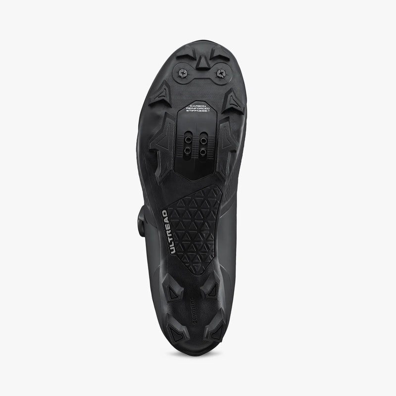 Bottom view of Shimano SH-XC503 ULTREAD rubber outsole showing lugged tread pattern, dual toe spike mounts, and recessed 2-bolt SPD cleat pocket