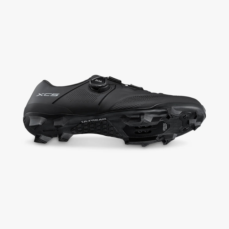 Angled dynamic view of black Shimano SH-XC503 shoe showing lower ULTREAD outsole tread lugs combined with the lateral BOA dial closure