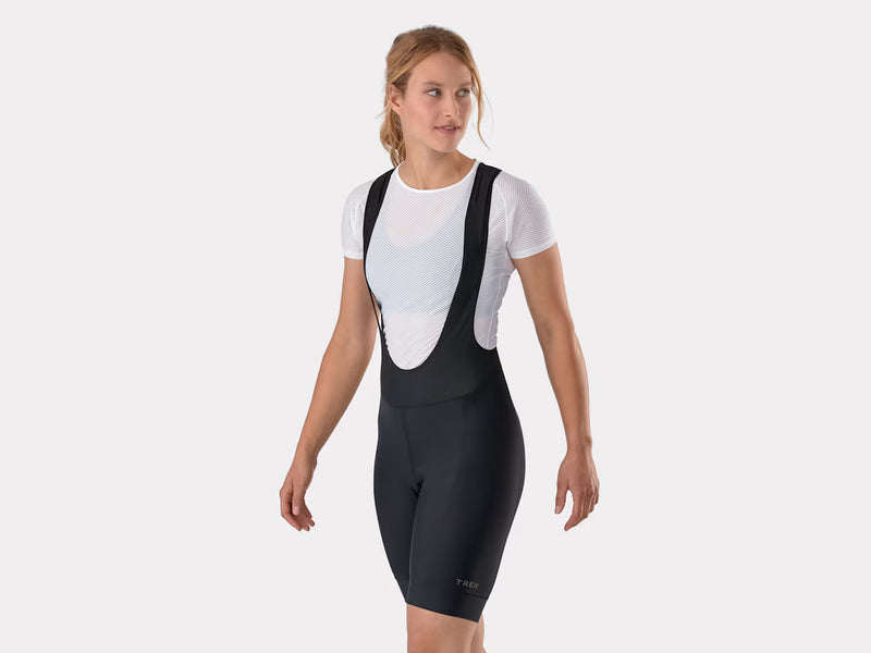 Three-quarter angled studio view of female model facing left in black Trek Solstice women's bib shorts, highlighting how the fitted shape and fabric drape in a riding posture