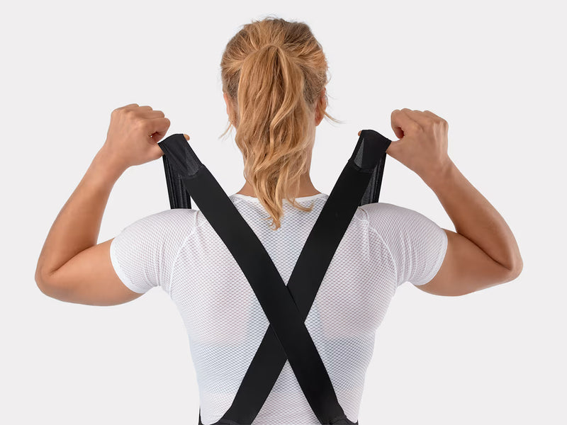 Close-up view of the upper back on the black Trek Solstice women's bib shorts as the model lifts the straps, detailing the shaped mesh crossover construction