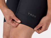 Close-up view of the lower left leg hem on the black Trek Solstice women's bib shorts, showcasing the compressive leg band stitching and prominent Trek logo