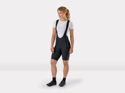 Full-length frontal studio view of female model standing in black Trek Solstice women's cycling bib shorts, showing the complete silhouette from head to toe
