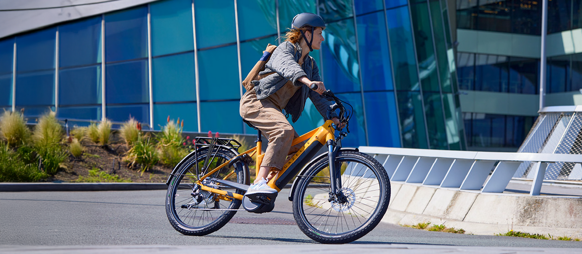 Person riding an electric bike on a city street with modern buildings in the background. / Personne roulant un vélo électrique dans une rue urbaine avec des bâtiments modernes en arrière‑plan.