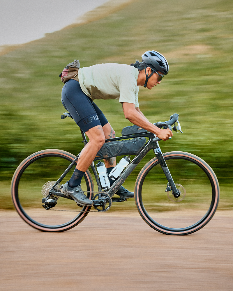Cyclist riding a road bike at high speed with mountains in the background, motion blur emphasizing speed. / Cycliste roulant à grande vitesse sur un vélo de route avec des montagnes en arrière‑plan, flou de mouvement accentuant la vitesse.