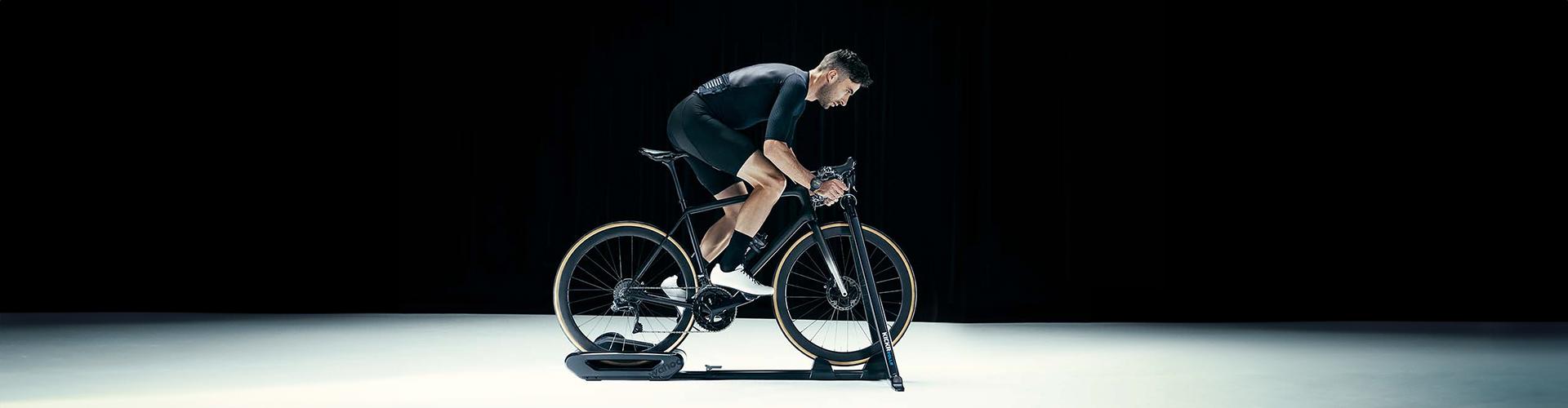 A man cycling indoors on a Wahoo KICKR ROLLR trainer in a well-lit studio setting, showcasing the equipment's sleek design and functionality.